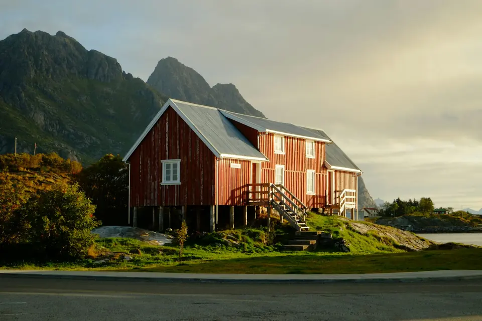 Rødt trehus på stolper i kveldslys med fjell i bakgrunnen